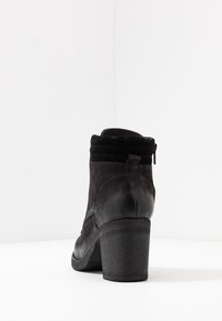 Botín negro con un diseño elegante, materiales de ante y cuero texturizado, cierre de cremallera en la parte trasera y tacón cuadrado.