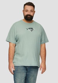 Lichtblauwe katoenen T-shirt met korte mouwen, ronde hals en een grafische print met de tekst "RIVERSIDE LODGE" op de voorkant.