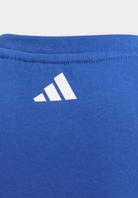 Camisa de algodón azul con una superficie texturizada y un logo blanco de Adidas que presenta tres franjas diagonales cerca del cuello.