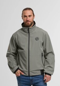 Grau weiche Shelljacke mit hohem Kragen, schwarzen Akzenten, Frontreißverschluss und zwei seitlichen Taschen. Mit einem Logo auf der Brust.
