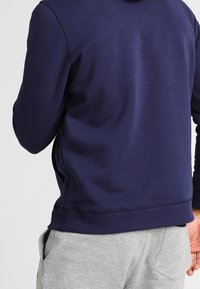 Felpa navy blu con una texture morbida e una vestibilità comoda, dotata di tasca a marsupio, polsini e orlo a costine, abbinata a pantaloni della tuta grigi chiari.