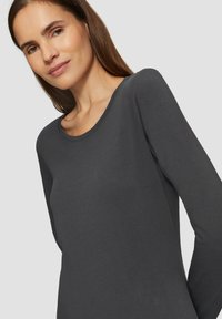 Donkere grijze top met lange mouwen, gemaakt van zacht en glad materiaal, met een ronde halslijn, een getailleerd ontwerp en een minimalistische stijl. Geen opvallende patronen of accenten.