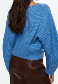 Blauer gerippter Pullover mit weiten Ärmeln, der ein strukturiertes Strickmuster aufweist. Kombiniert mit dunklen, eleganten, hoch taillierten Hosen.