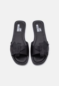 Μαύρα σανδάλια Moschino με επίπεδη σόλα και διακοσμητικά επικαλυπτόμενα λουριά στολισμένα με μαύρους στρας.