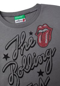 Gray cotton t-shirt featuring black text, a red and silver rhinestone lips design, and black star accents near the neckline.