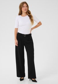 Haut blanc à rayures avec des manches courtes associé à un pantalon noir à jambe large avec une ceinture dotée d'une boucle en D argentée et un tissu texturé. Talons noirs.