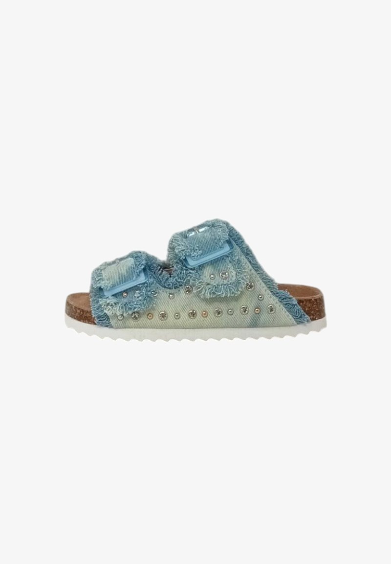 Sandale à glissière en denim bleu avec des bords effilochés, deux straps ajustables, des clous décoratifs et une semelle intérieure en liège texturé, dotée d'une semelle en caoutchouc blanche.