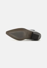 Zapato de tacón alto con un upper de cuero gris texturizado, puntera afilada y tacón negro cuadrado. Presenta acentos decorativos en el lateral.