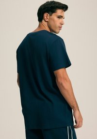 Granatowa bawełniana koszulka z krótkim rękawem, o luźnym kroju i okrągłym dekolcie, pokazana od tyłu, w zestawieniu z dopasowanymi spodniami.