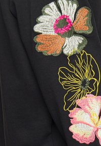 Tela negra con bordado floral colorido. Presenta grandes flores en blanco, naranja, rosa y amarillo con un detallado bordado.