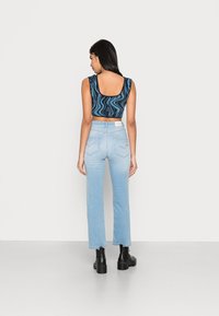 Top cropped azul com padrão e costas em forma de colher, combinado com jeans de cintura alta azul claro e botas de tornozelo pretas. Detalhes de design notáveis incluem costura.