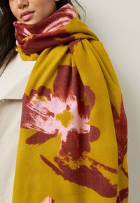 Lillemustriga sall kollases toonis roosade ja burgundi varjunditega, valmistatud pehmest kangast, stiilselt kaela ümber laotud.