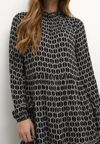 Abito a righe in bianco e nero con un design geometrico, caratterizzato da un collo alto arricciato e maniche lunghe con polsini elasticizzati.