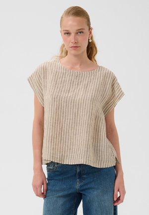Vrouw met een lichte huid en blond haar die pareloorbellen draagt, een beige-wit gestreept shirt met korte mouwen en blauwe spijkerbroek.