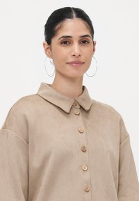 Beige, suede-like shirt in a relaxed fit with a collar, button front, and wooden buttons. Features loose sleeves and a smooth texture.