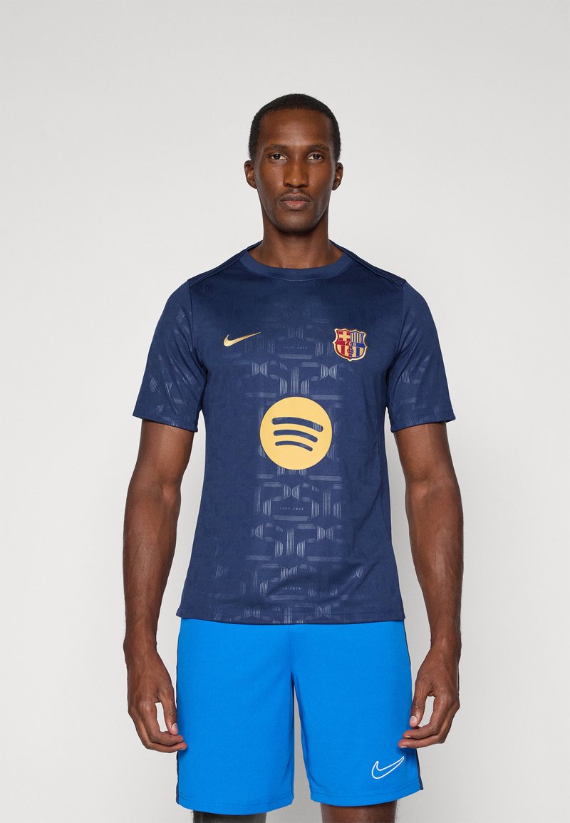 Camiseta de fútbol Nike de color azul marino con un patrón texturizado, que presenta un logo dorado de Spotify y un escudo del FC Barcelona, combinada con pantalones cortos azules.