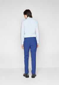 Lichtblauwe overhemd met lange mouwen, slanke pasvorm, met een knoopsluiting bij de kraag, gecombineerd met strakke blauwe broek. Zwarte schoenen, gladde stof en een op maat gemaakt ontwerp.
