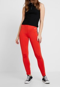 Röda leggings med en åtsittande design och sidostrecken, ihopparade med en svart ärmlös topp. Tillverkade av bomull med en slät textur. Svarta sneakers.