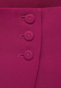 Fuchsiová blůza s třemi kulatými knoflíky potaženými tkaninou a hladkým, texturovaným povrchem. Geometrický design límce s čistými liniemi.