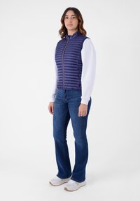 Gilet in piuma navy con cuciture orizzontali, colletto alto e zip frontale, abbinato a jeans blu a zampa d'elefante e sneakers bianche.