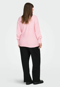 Lys rosa ribbestrikket genser med lange ermer, kombinert med svarte bukser med vide ben og kraftige svarte sko, sett bakfra.