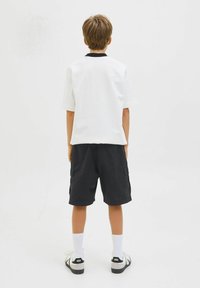 Chemise blanche à manches courtes avec un col noir, associée à un short cargo noir. Portée avec des chaussettes blanches et des chaussures noires à enfiler.