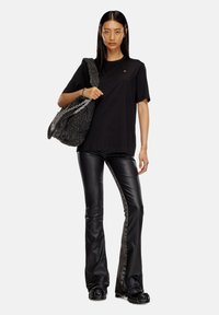 T-shirt noir, coupe ample ; pantalon en cuir noir évasé avec des panneaux latéraux gris ; sac à main noir matelassé avec une bandoulière en chaîne.
