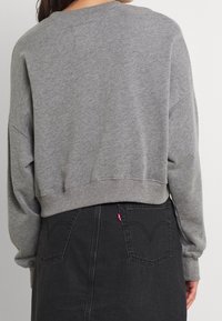 Sweat-shirt gris court avec poignets et ourlet côtelés, présentant une coupe décontractée. Associé à une jupe en denim noire avec deux poches arrière.