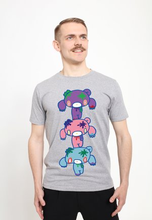 Uomo con i baffi che indossa una maglietta grigia con orsi dei cartoni animati impilati in viola, rosa e blu con schizzi colorati.