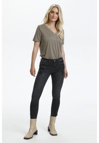 T-shirt gris à col en V avec des manches courtes, jean skinny en denim foncé avec des détails en zip, et bottines beige à talon bas.