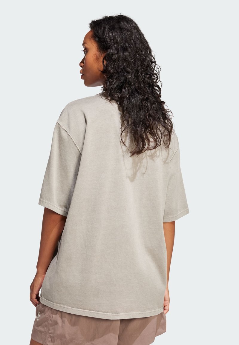 Camiseta gris claro de gran tamaño hecha de tela suave. Mangas cortas, dobladillo redondeado, diseño minimalista sin logotipos ni adornos visibles.