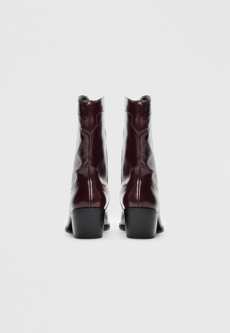 Stivali in pelle bordeaux alla caviglia con un design elegante, dotati di tacco a blocco e dettagli di cucitura evidenti sul retro.