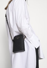 Svart läder crossbody-väska med en strukturerad form, texturerad yta och detaljer i guldfärg, hängande från en kedjerem.