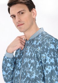 Giacca bomber con un motivo astratto blu e grigio, collo e polsini a costine, chiusura frontale con zip e orlo elasticizzato.