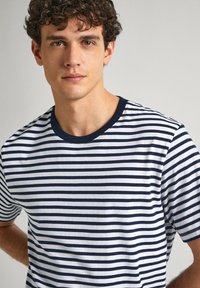 Dryžuota medvilninė marškinėliai su horizontaliomis tamsiai mėlynomis ir baltomis juostelėmis, apvali kaklo iškirpė, laisvas fasonas. Textūruotas audinys su glotnia apdaila.