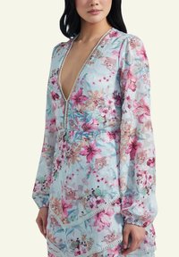 Floral patterned dress in light blue fabric, with long sleeves, deep V-neck, and lace trim detailing. Features a tiered skirt design.