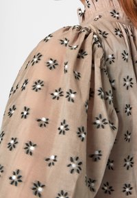 Vaaleankermanvuori, jossa on puffihihat, mustaa kukkakirjontaa ja valkoisia detaileja. Raskaampaa kangasta, jossa on röyhelökaulus.