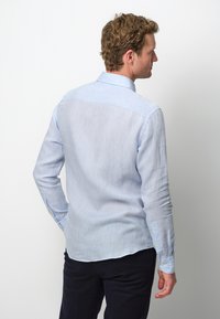 Camicia a maniche lunghe di colore azzurro chiaro con una texture morbida, polsini con bottone e orlo arrotondato. Presenta un design semplice e pulito con una vestibilità su misura.