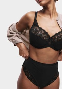 Schwarze Spitzen-Bralette mit gewellten Kanten, kombiniert mit hochgeschnittenen schwarzen Unterhosen. Verfügt über transparente Mesh- und dekorative Spitze-Details.