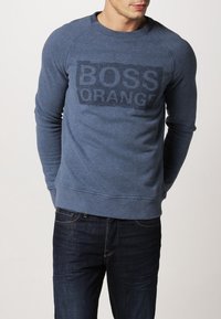 Sudadera azul hecha de un tejido suave con cuello redondo, que presenta un estampado texturizado del logo "BOSS ORANGE" en el frente y puños acanalados.