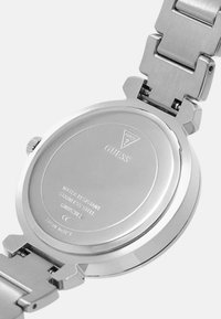 Roestvrijstalen horloge met een gepolijste case-back, voorzien van een gegraveerd merklogo en specificaties, waaronder waterbestendigheid.