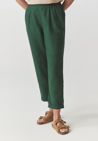 Pantalons en lin vert avec une coupe décontractée, dotés d'une taille froncée et de poignets retroussés, associés à des sandales en daim marron.