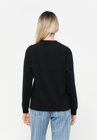 Black long-sleeve sweatshirt with ribbed cuffs and round neckline. Smooth cotton fabric. Worn with light blue vertical-striped jeans.