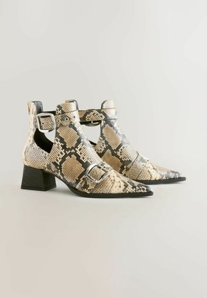 Karein kärjellinen nilkkuri vaaleanbeige ja mustassa käärmeennahkakuosissa, jossa on solkivetimien yksityiskohtia, teksturoitu pinta ja tukeva musta korko.