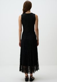 Robe noire avec un haut ajusté sans manches et une jupe en dentelle fluide. La jupe présente des motifs floraux complexes et un design en couches.