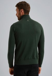 Dunkelgrüner Pullover mit hohem Kragen und gerippten Bündchen. Taillierte Passform, weicher Stoff und ein kleines Logodetail in der Nähe des Kragens.