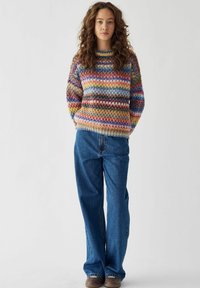 Gekleurde gebreide trui met een grof textuur, met horizontale strepen in blauw, roze, geel en bruin. Combinatie met wijde jeans.