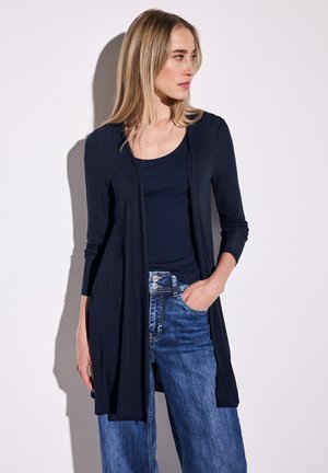 Cardigan lungo navy con apertura frontale, texture a coste e maniche lunghe, abbinato a una maglia navy e jeans a gamba larga blu.