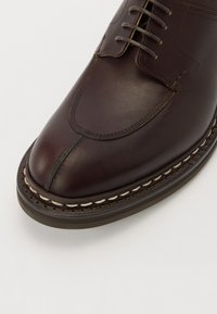 Czarne skórzane buty z zaokrąglonym noskiem i stębnowanymi detalami. Posiadają sznurowane zapięcie oraz kontrastowe jasne przeszycie wzdłuż podeszwy.