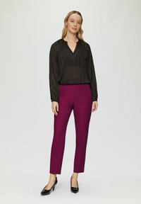 Blouse noire à rayures à manches longues avec un décolleté en V, associée à un pantalon violet ajusté. Mannequin portant des talons noirs ; arrière-plan neutre.